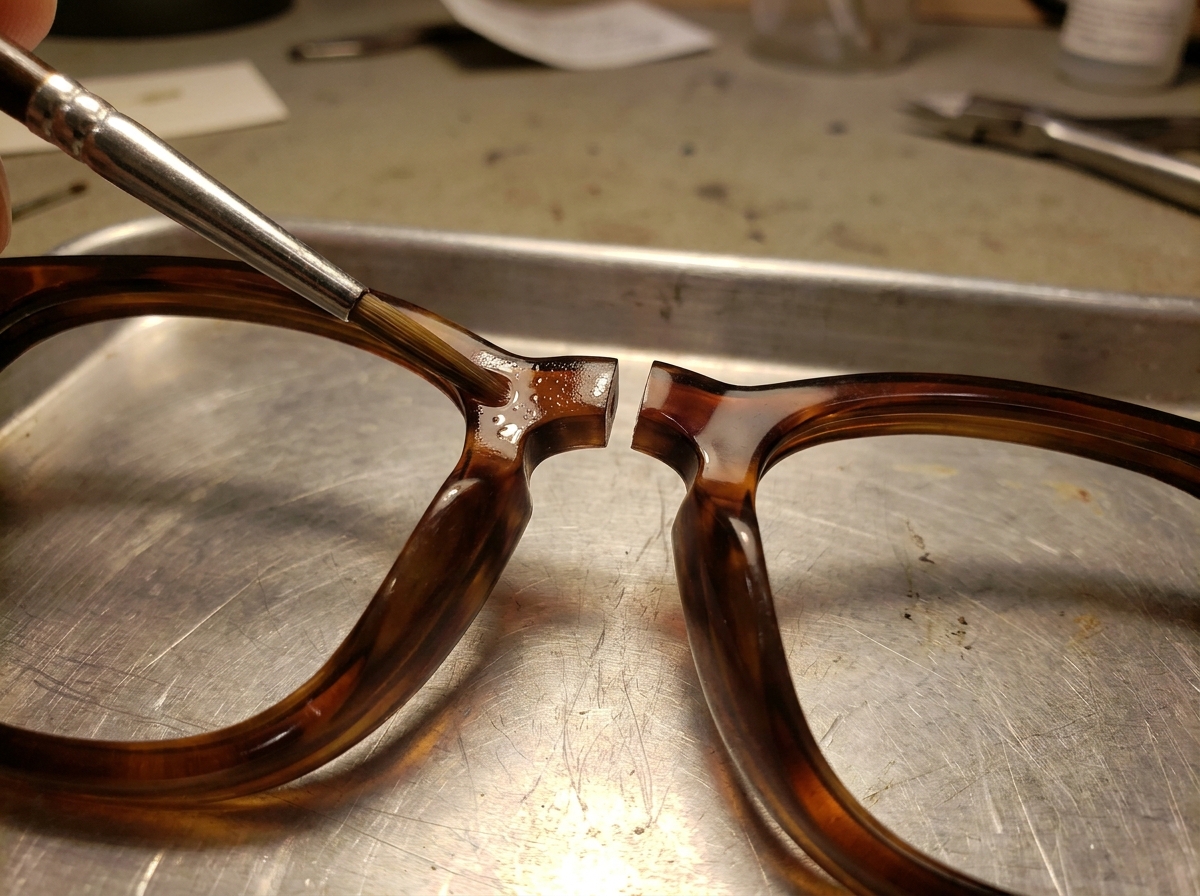 Zwei Acetat-Bruchkanten einer Brille werden mit Lösemittel benetzt kurz vor dem Zusammenfügen.