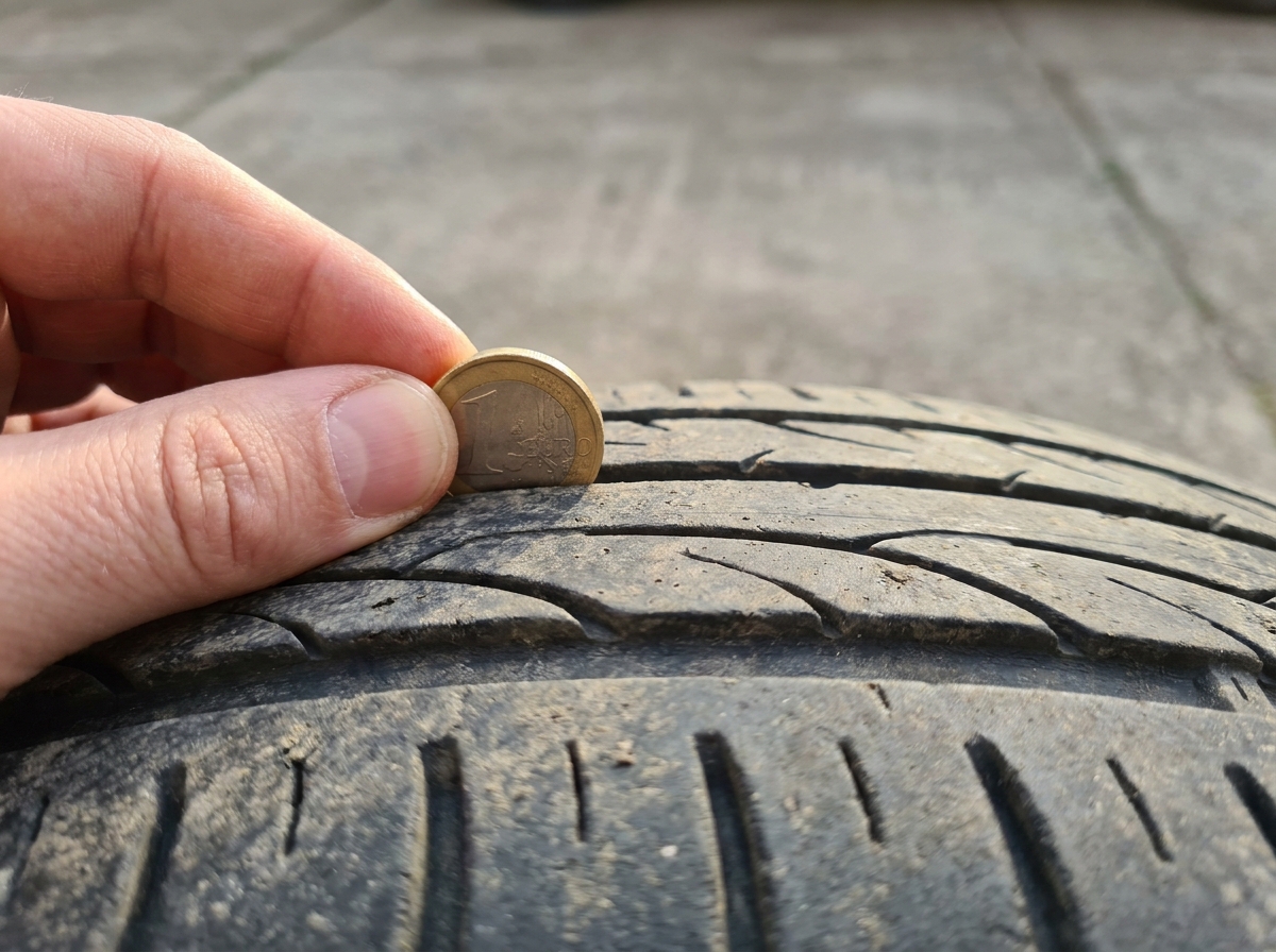 Eine-Euro-Münze wird zur Profiltiefenprüfung in eine Reifenrille eines Autoreifens gehalten